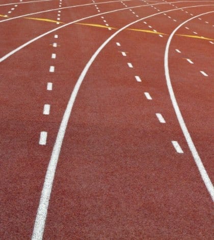 Parallel lanes curve around outdoor running track with artificial, all-weather surface