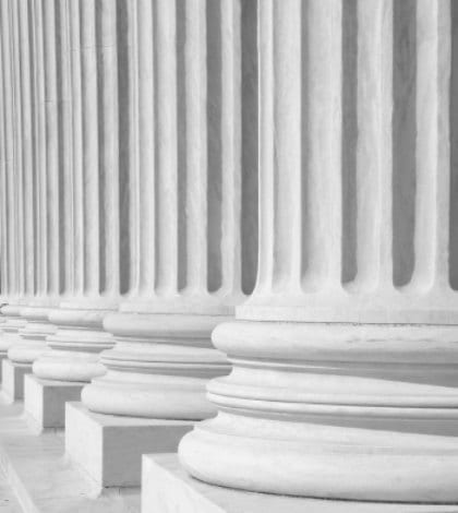A row of columns at the entrance to the US Supreme Court in Washington, DC.

Completed in 1935, the US Supreme Court building in Washington, DC, is the first to have been built specifically for the purpose, inspiring Chief Justice Charles Evans Hughes to remark, “The Republic endures and this is the symbol of its faith.”

The Court was established in 1789 and initially met in New York City. When the national capital moved to Philadelphia, the Court moved with it, before moving to the permanent capital of Washington, DC, in 1800. Congress lent the Court space in the new Capitol building, and it was to change its meeting place several more times over the next century, even convening for a short period in a private house after the British set fire to the Capitol during the War of 1812.

The classical Corinthian architectural style was chosen to harmonize with nearby congressional buildings, and the scale of the massive marble building reflects the significance and dignity of the judiciary as a co-equal, independent branch of government.

The main entrance is on the west side, facing the Capitol. On either side of the main steps are figures sculpted by James Earle Fraser. On the left is the female Contemplation of Justice. On the right is the male Guardian or Authority of Law. On the architrave above the pediment is the motto “Equal Justice under Law.” Capping the entrance is a group representing Liberty Enthroned, guarded by Order and Authority, sculpted by Robert Aitken.

At the west entrance are marble figures sculpted by Hermon A. MacNeil. They represent great law givers Moses, Confucius, and Solon, flanked by Means of Enforcing the Law, Tempering Justice with Mercy, Settlement of Disputes between States, and Maritime and other functions of the Supreme Court. The architrave carries the motto “Justice the Guardian of Liberty.”

The interior of the building is equally filled with symbolic ornamentation. The main corridor is known as the Great Hall and contains double rows of marble columns and busts of all former chief justices. At its east end, oak doors open into the Court Chamber, where the justices preside. Most of the second floor is devoted to office space. The library occupies the third floor and has a collection of more than 450,000 volumes. 

The Supreme Court consists of the Chief Justice of the United States and eight Associate Justices. The term of the Court begins on the first Monday in October and lasts for the full year. Approximately 8,000 petitions are filed with the Court each term. A further 1,200 applications of various kinds are filed that can be acted upon by a single justice. 

The Supreme Court has appellate jurisdiction except “in all Cases affecting Ambassadors, other public ministers and Consuls, and those in which a State shall be Party” (Constitution, art. III, §2), for which it has original jurisdiction. Congress has also from time to time conferred on the Supreme Court the power to prescribe rules of procedure to be followed by the lower courts.