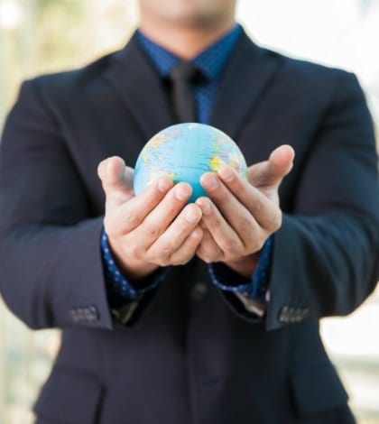 Closeup of a man wearing a suit and holding a small globe in his hands