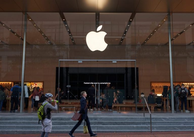 Portland, Oregon, USA - Oct 1, 2019: A man strides past an Apple Store in downtown Portland. The big screen inside is seen advertising Apple's fastest A13 Bionic chips in the new iPhone series.