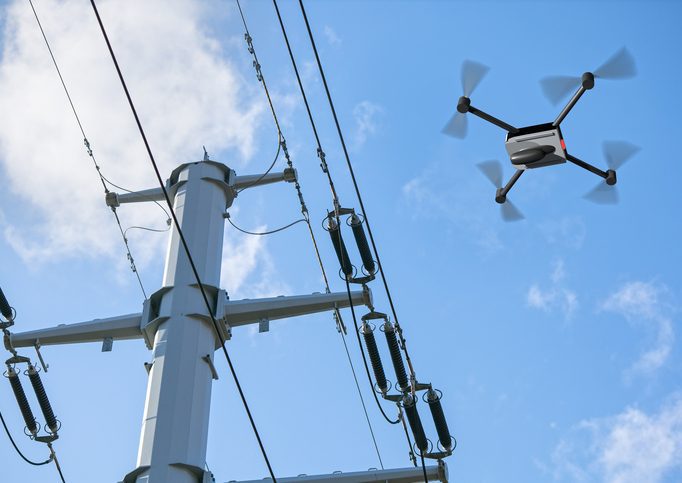 Electric wires on poles with drone hovering above them.