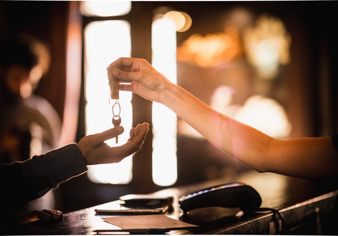 Somebody's arm over a desk dropping a key into the hand of another arm over the desk.