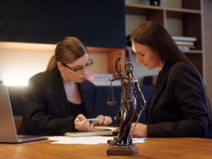 legal team of two women with a bronze woman holding scales of justice on desk in foreground