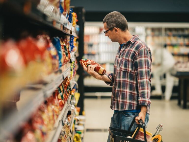 man-reading-a-label-while-grocery-shopping-in-a-supermarket-aisle UNFI Cyberattack Poses Supply Chain Risk to Whole Foods, Other Grocers