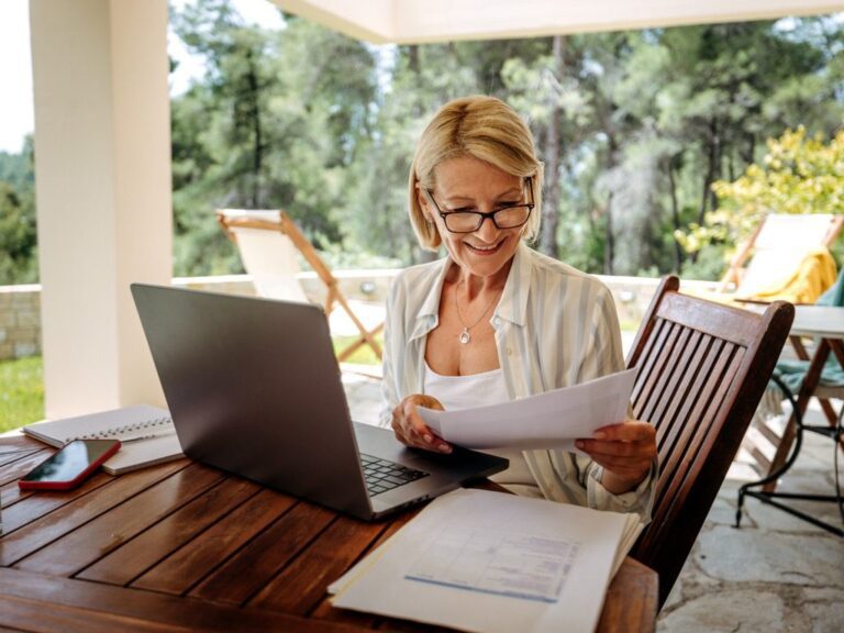 smiling woman in retirement viewing laptop in sunny backyard